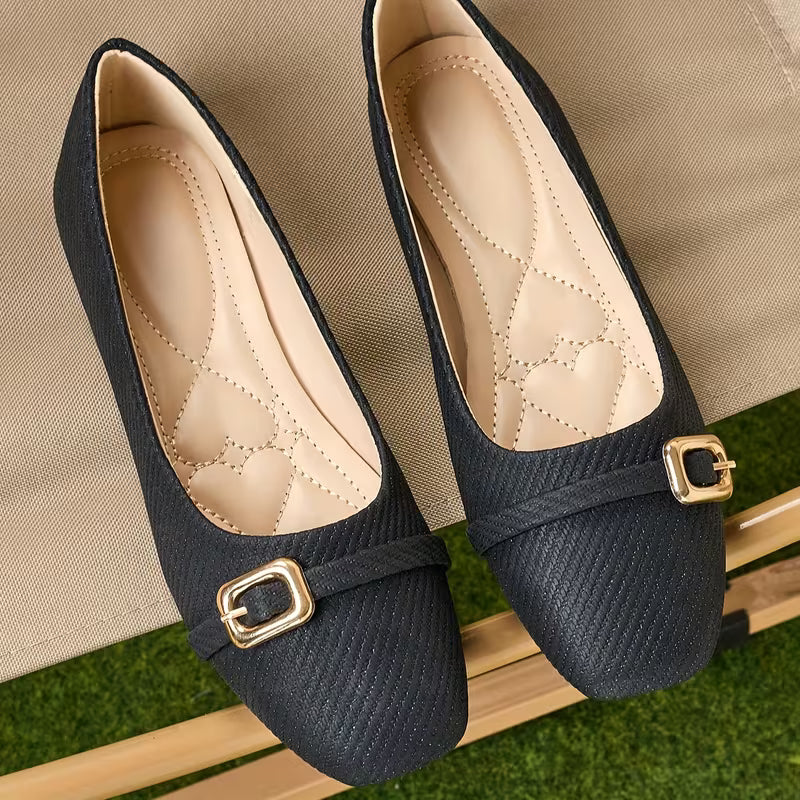 Pair of navy blue shoes with gold buckles on a beige surface.