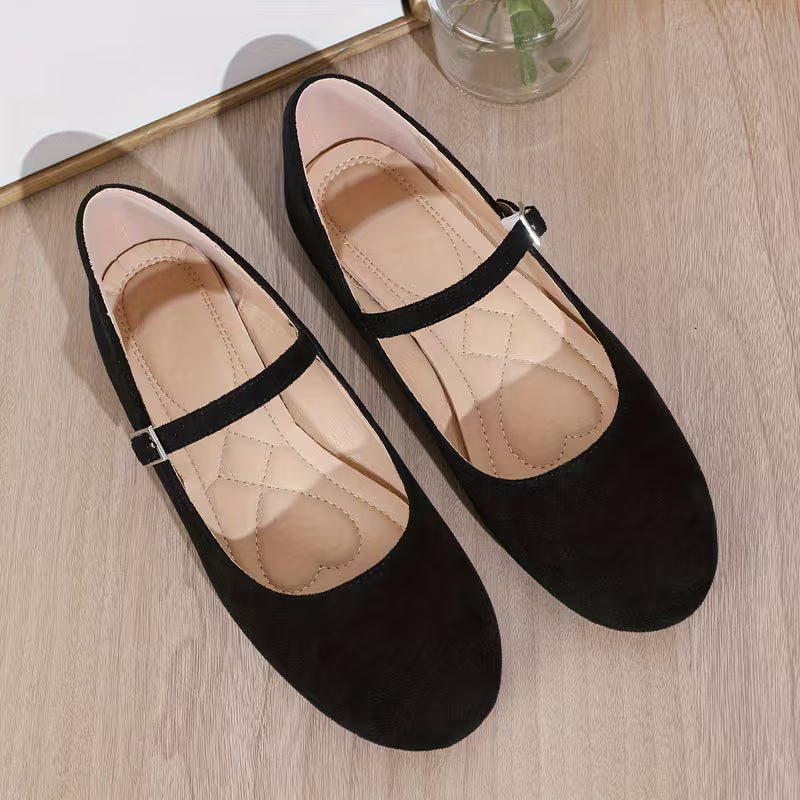 Black flat shoes with a strap on a light wooden surface