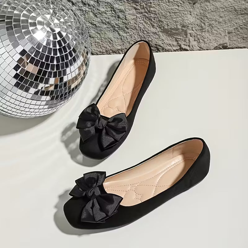 Black shoes with bow details on a light surface next to a disco ball.