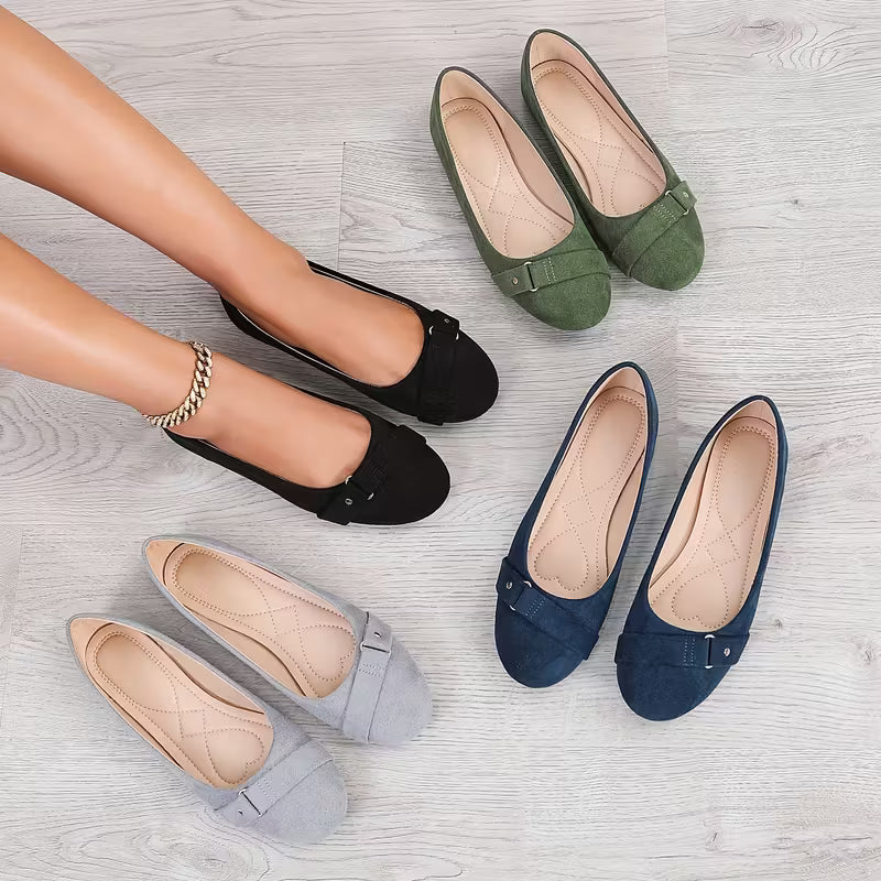 Four pairs of flat shoes in black, green, blue, and beige on a light wooden floor.