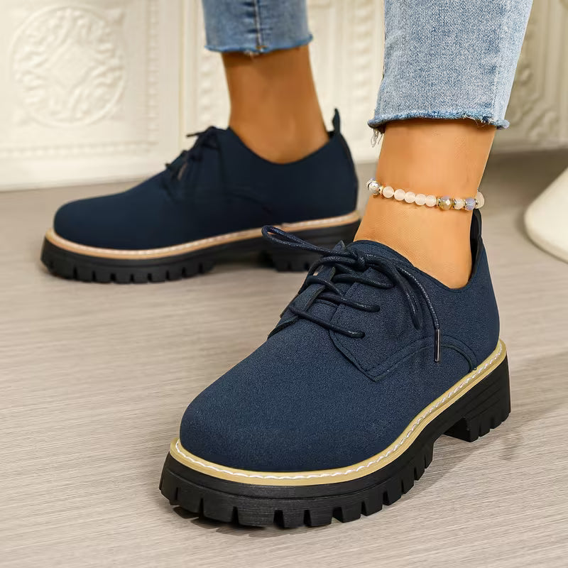 Navy blue shoes with thick soles worn by a person on a light wooden floor.