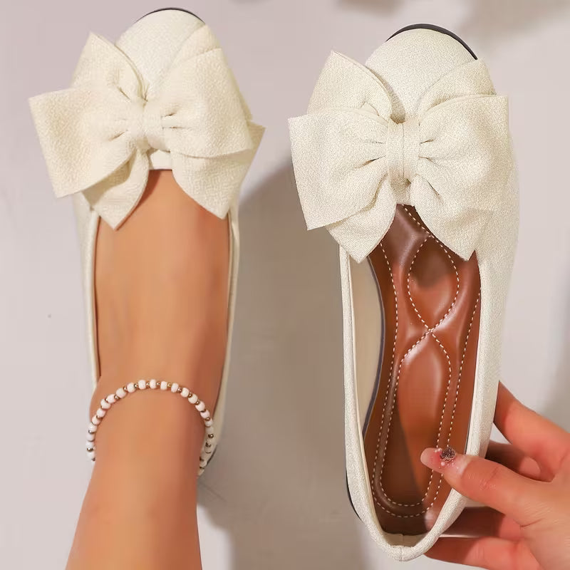 White flats with large bows held by a hand against a neutral background