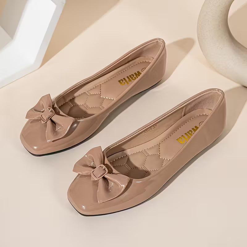 Pair of beige flat shoes with bow details on a light background