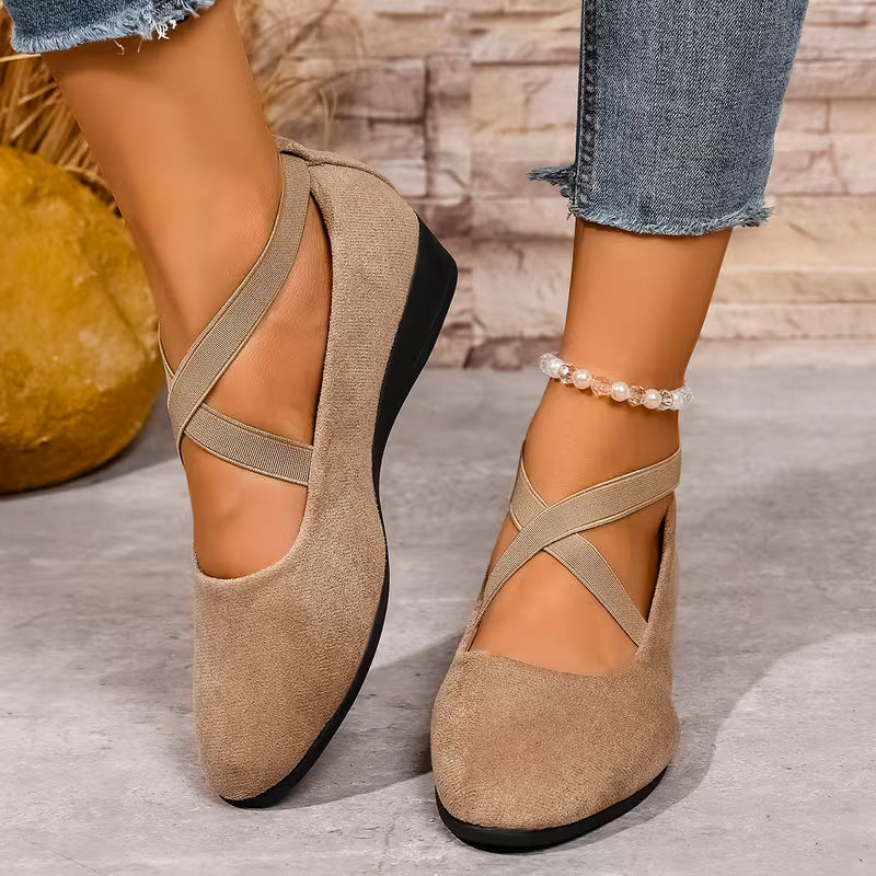 Beige suede shoes with cross straps worn by a person on a stone surface.