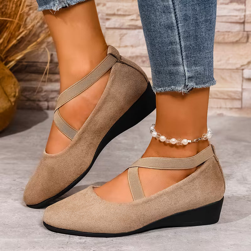 Beige flat shoes with thin straps worn by a person on a stone floor.