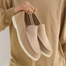 Person holding a pair of beige loafers against a neutral background