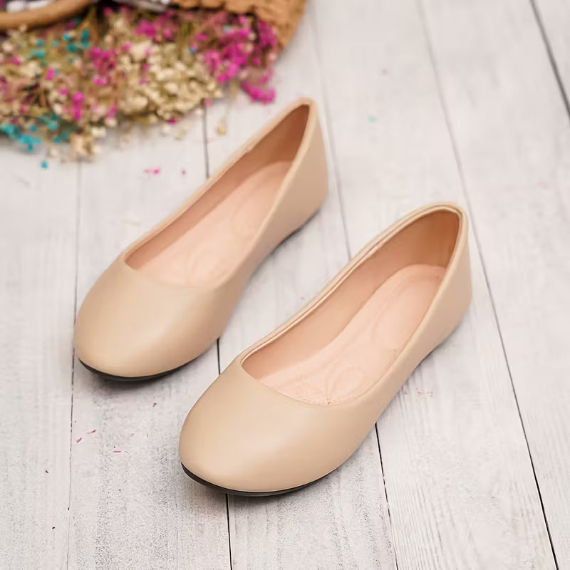 Pair of beige flat shoes on a light wooden floor with flowers in the background