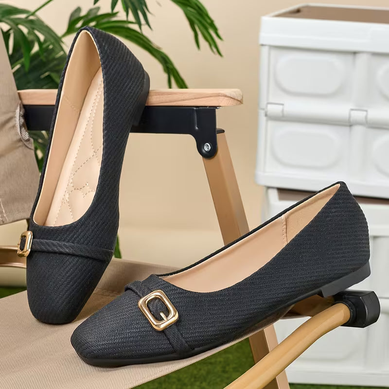 Black shoes with gold buckles on a chair with a neutral background