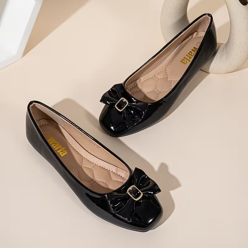 Black patent leather shoes with bow details on a beige surface