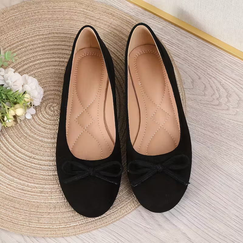 Pair of black suede shoes with bow details on a textured surface.