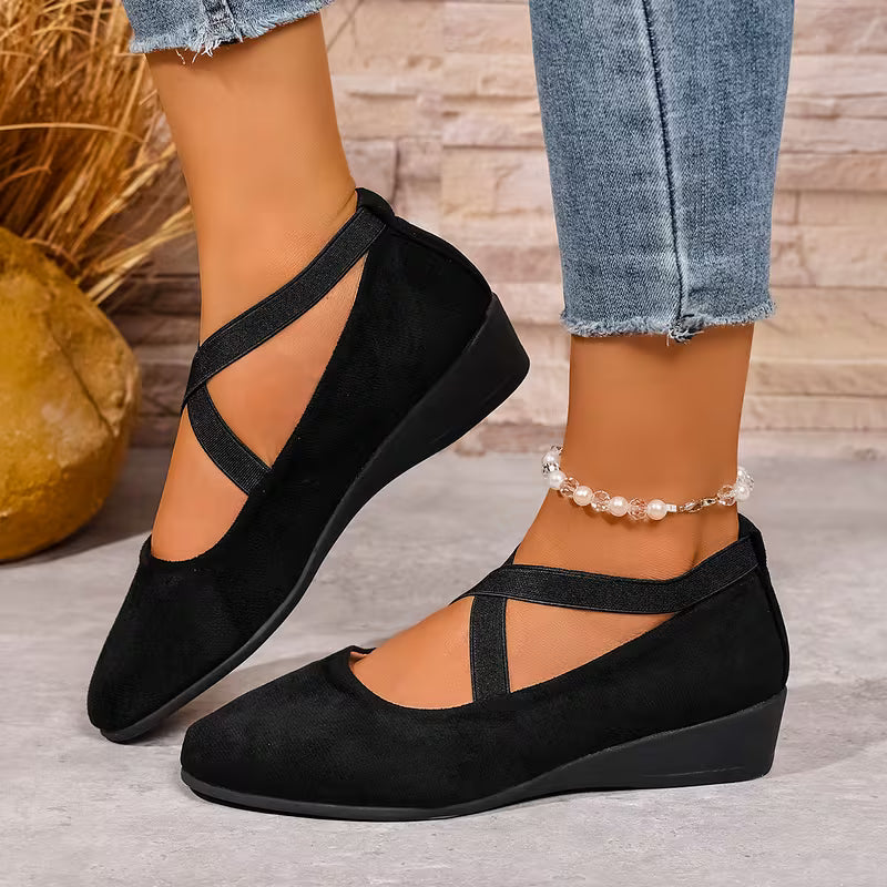 Black wedge sandals worn with jeans on a wooden floor.