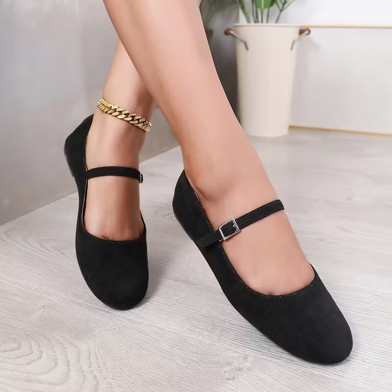 Black flat shoes worn by a person on a light wooden floor.