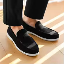 Black loafers worn with black pants on a wooden floor