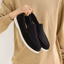 Person holding a pair of black loafers with white soles against a neutral background
