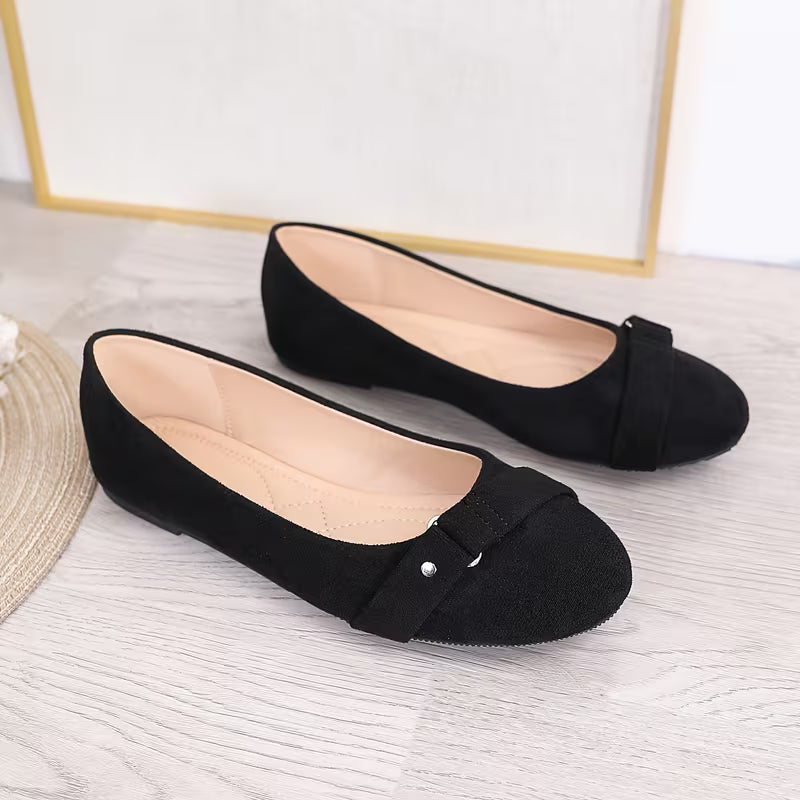 Black flat shoes with a bow on a light wooden floor.