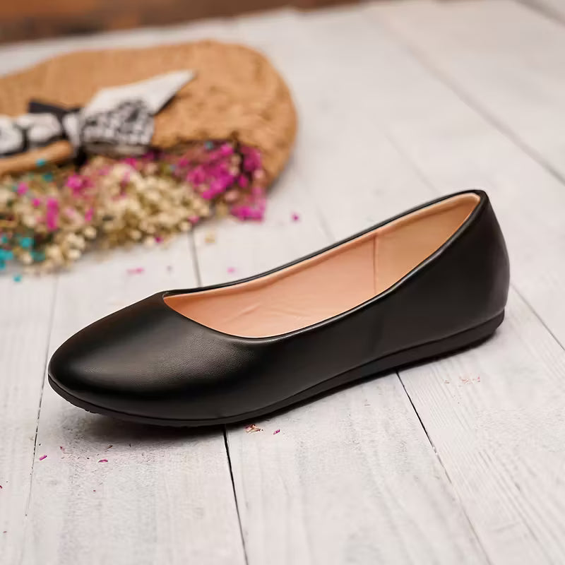 Black flat shoes on a light wooden floor.