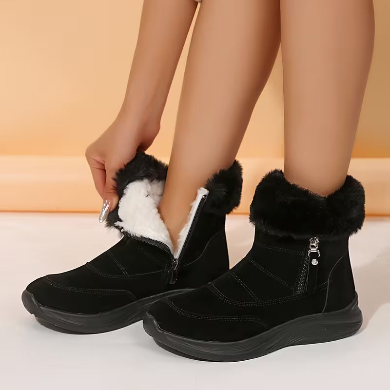 Black winter boots with fur trim being worn on a light background