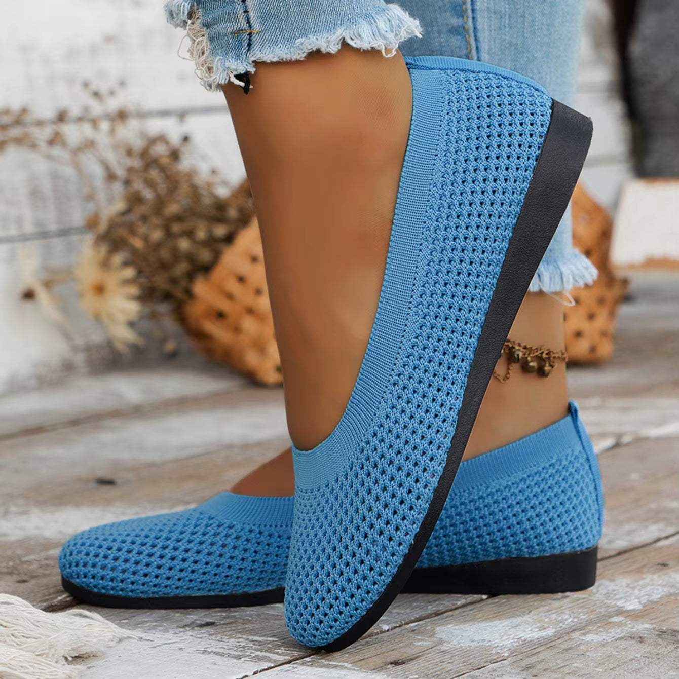 Blue textured shoes with black soles worn by a person on a wooden floor.
