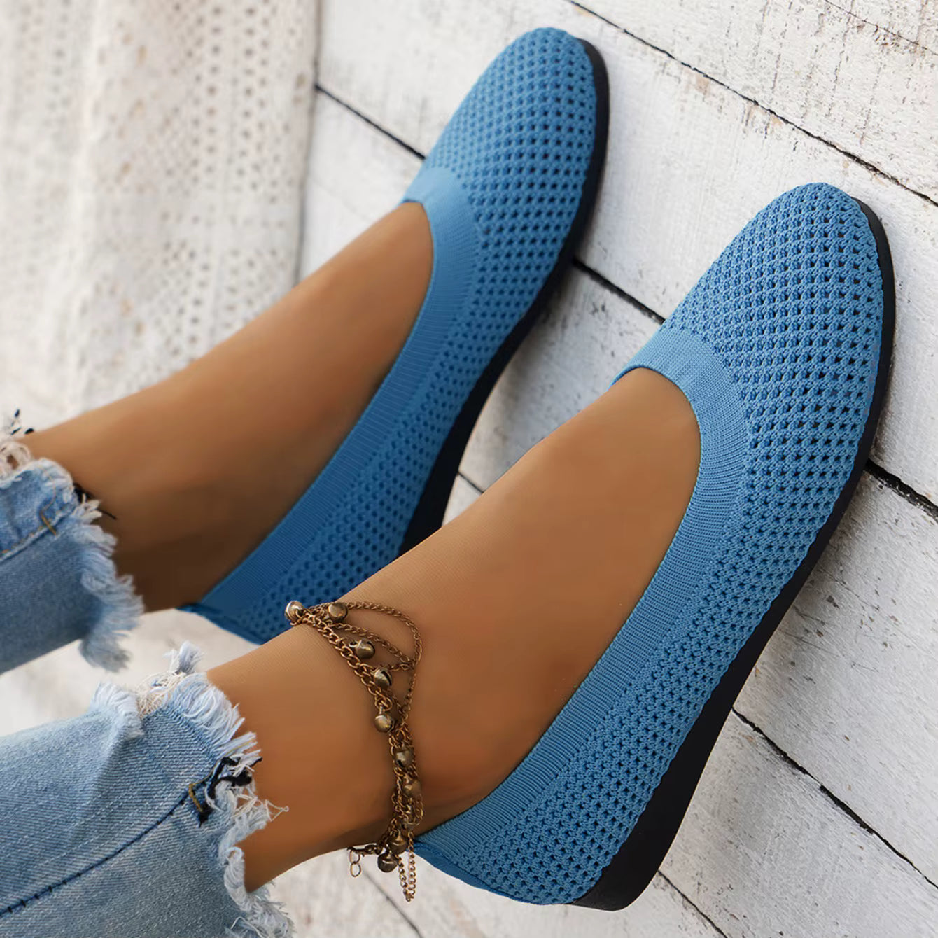 Blue flats worn with denim jeans on a light wooden floor.
