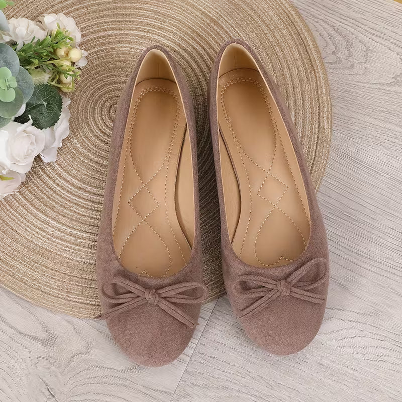 Pair of brown shoes with bow details on a textured surface with flowers and a hat.