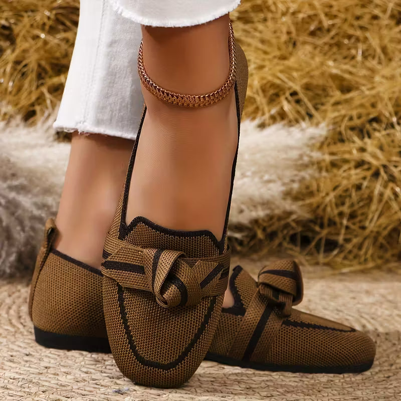 Brown loafers with knitted design worn by a person on a textured surface.