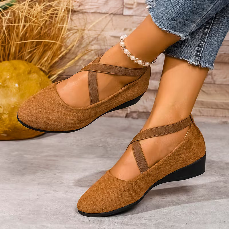 Brown shoes with straps worn by a person on a gray surface with a textured wall background