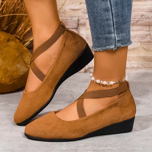 Brown wedge shoes worn with rolled-up jeans on a neutral background