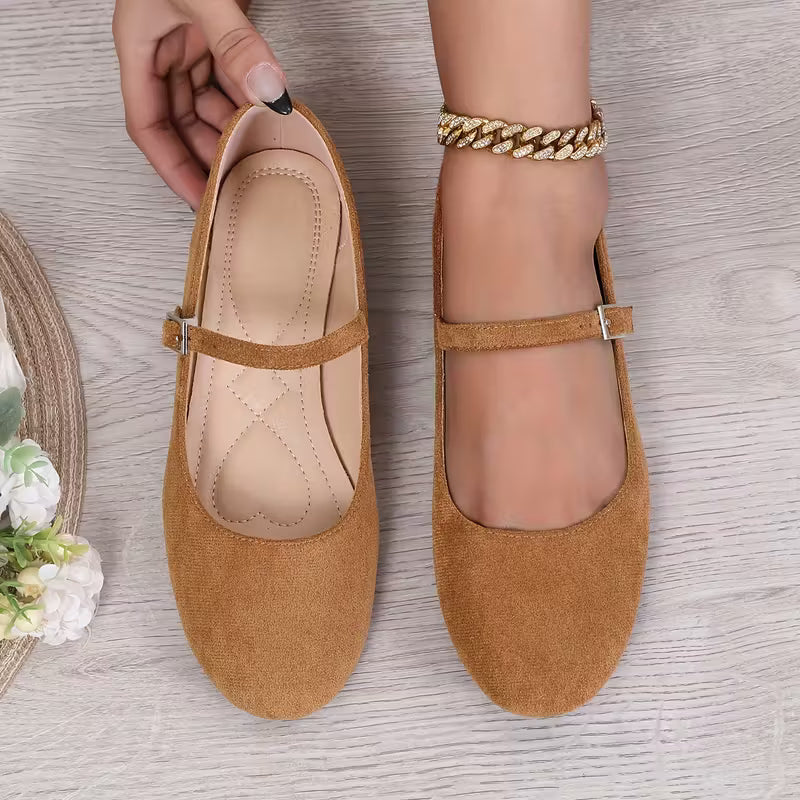 Brown flat shoes with a strap on a wooden surface