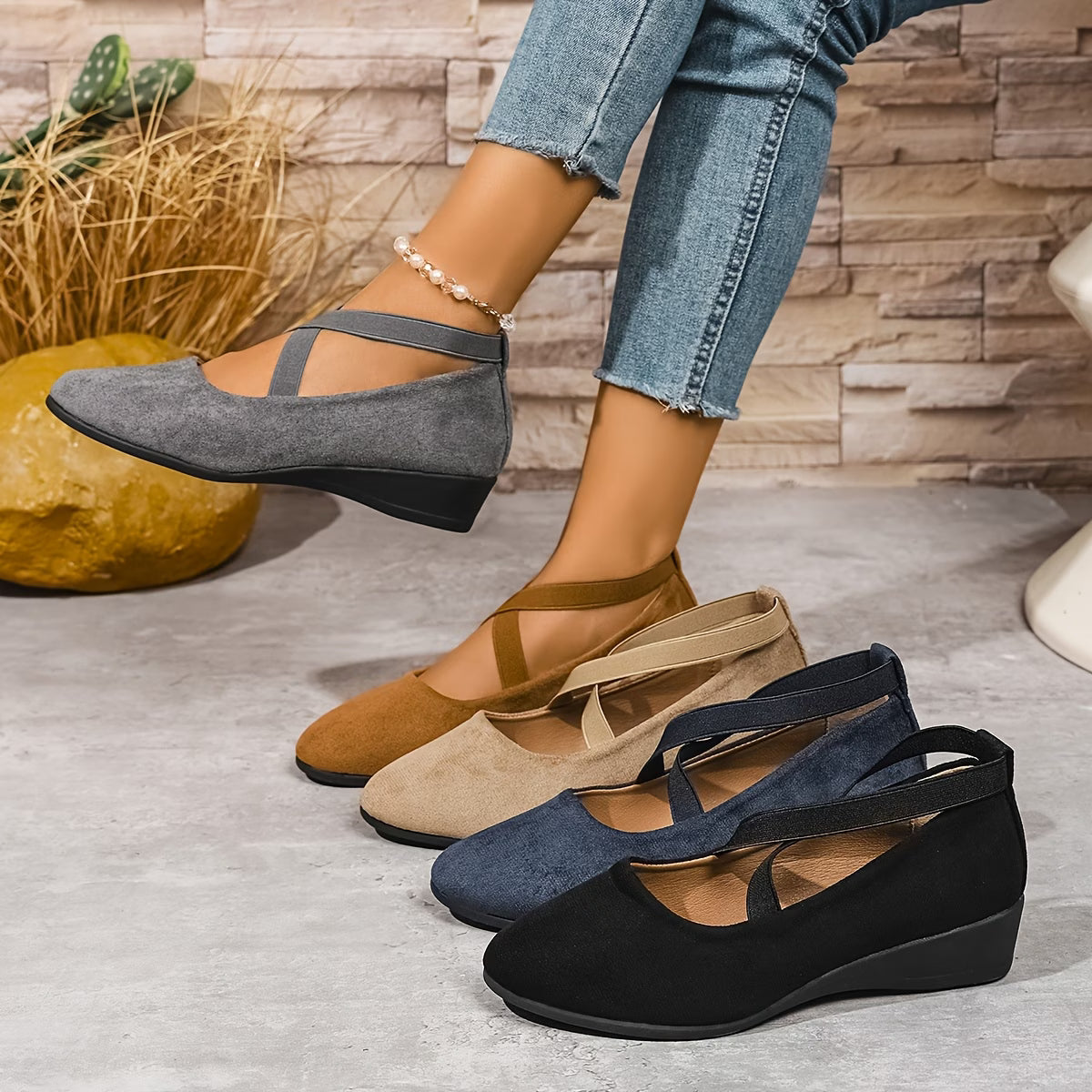 Four pairs of women's wedge sandals in different colors on a concrete floor with a stone wall background.