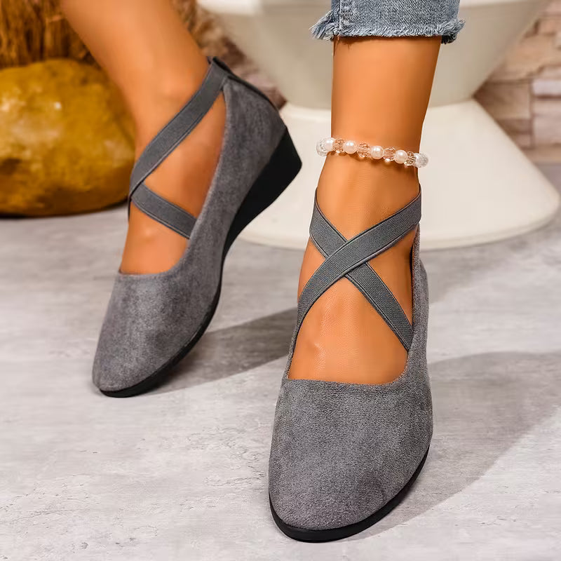 Gray suede shoes with cross straps worn by a person on a light wooden floor.