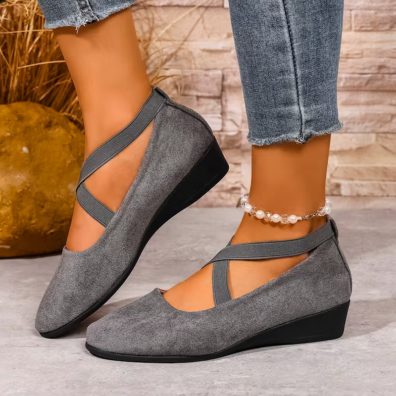 Gray wedge shoes worn with denim jeans on a neutral background