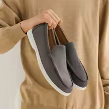 Person holding a pair of gray loafers against a plain background