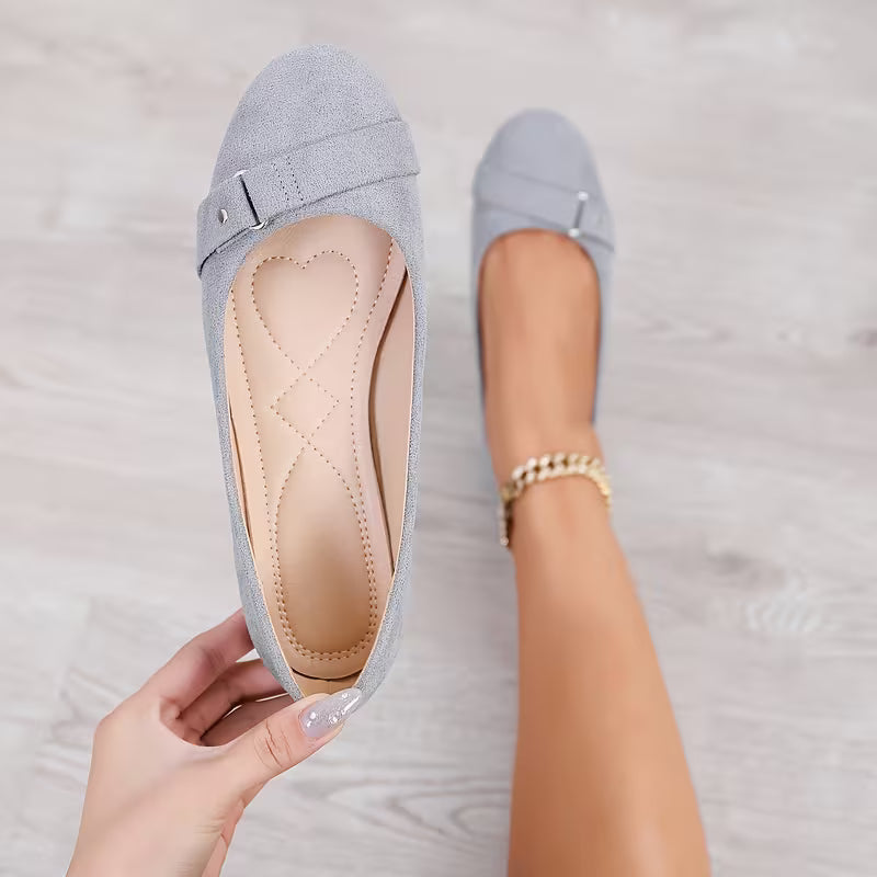 Light blue flat shoes with a hand holding one shoe, on a light wooden floor.