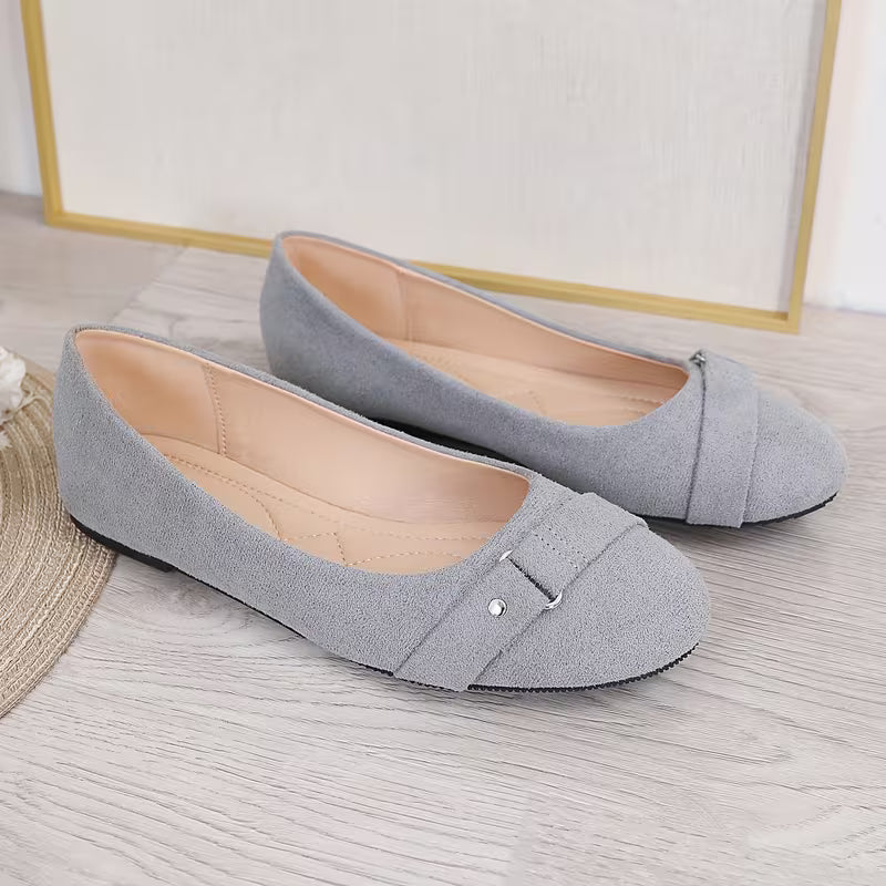Pair of gray flat shoes with a strap on a light wooden floor.