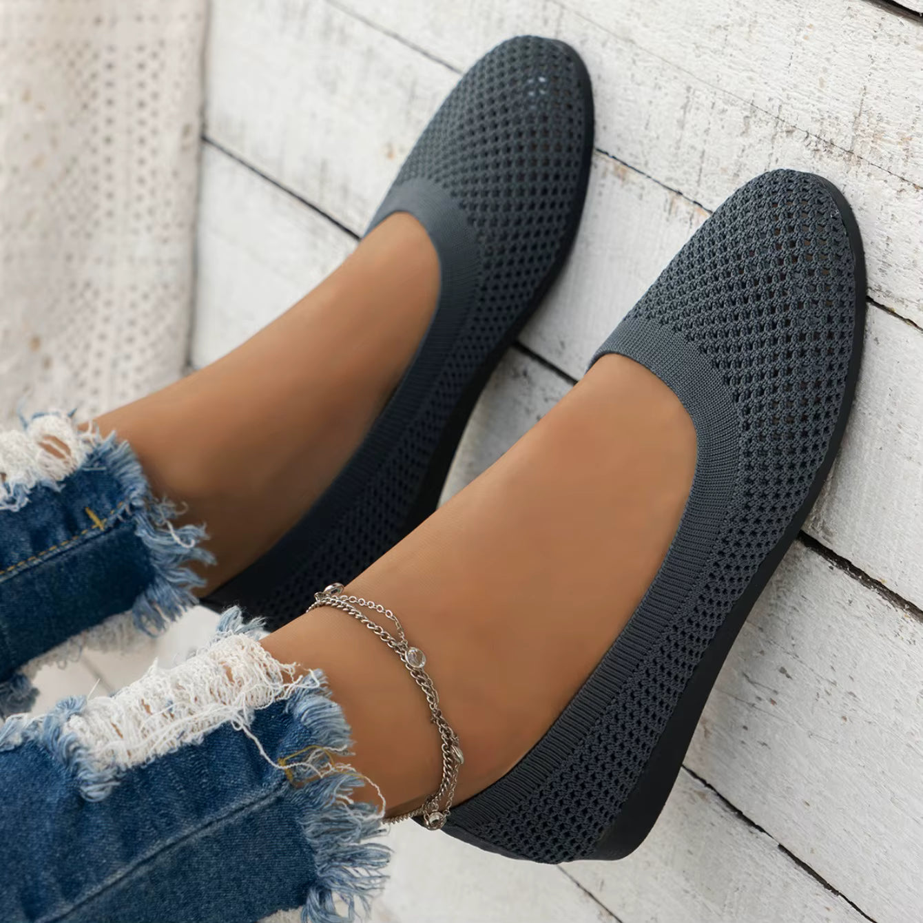 Black woven flats worn with denim jeans on a light wooden floor.