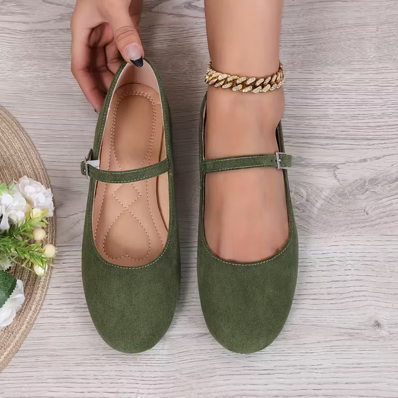 Green flat shoes with a strap held by a hand on a wooden surface.