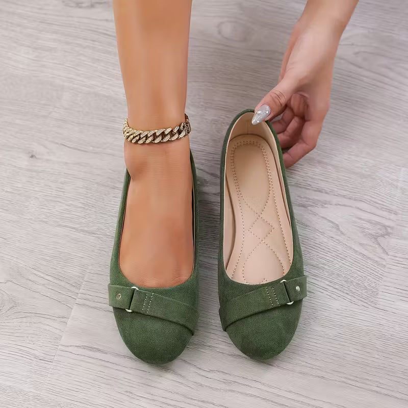 Green flat shoes with a buckle on a gray wooden floor.