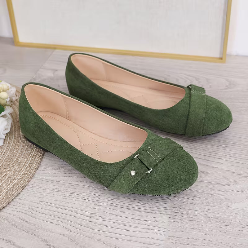 Green flat shoes with a buckle on a light wooden floor.