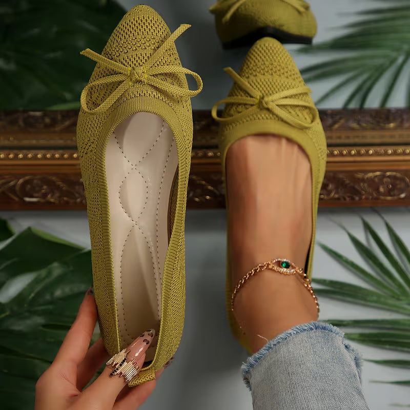 Green knitted shoes with a bow held by a hand against a decorative background