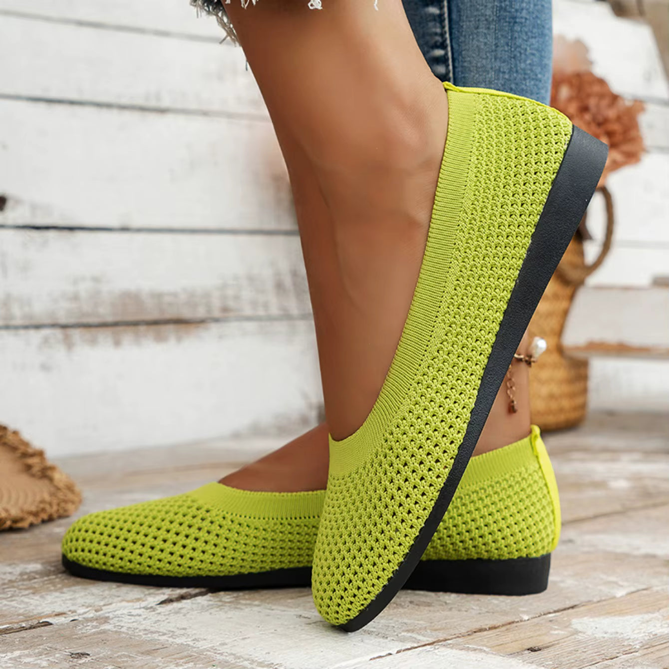 Green knitted shoes with black soles on a wooden floor.