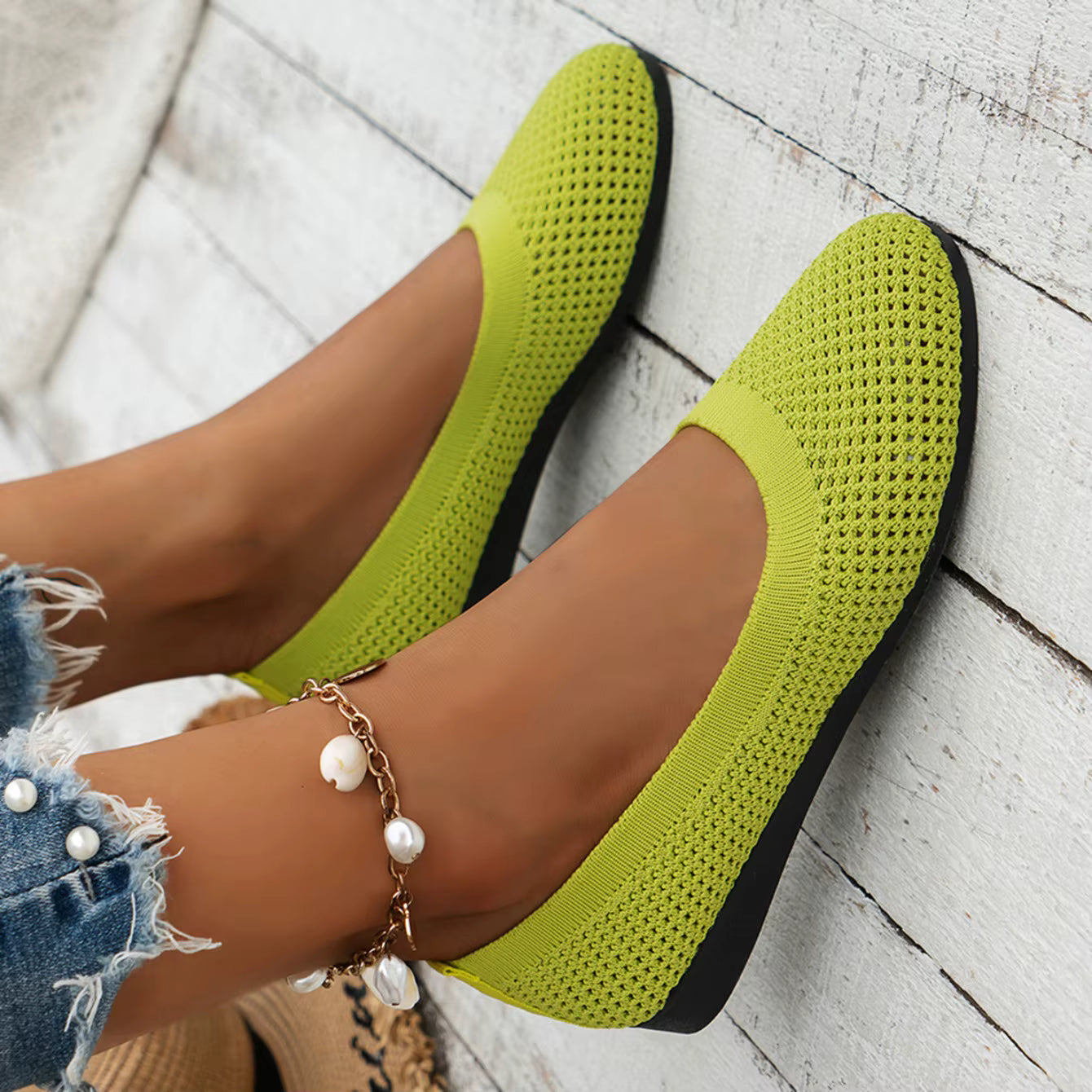 Green flat shoes worn with a denim skirt on a wooden floor.