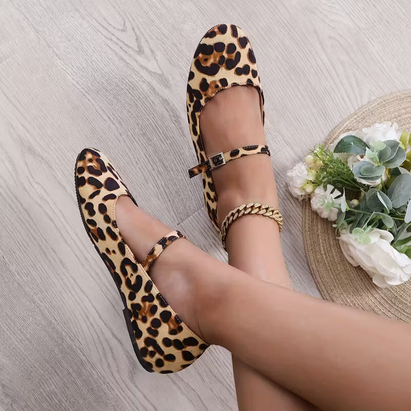 Leopard print shoes worn by a person on a light wooden floor with a decorative mat and flowers.