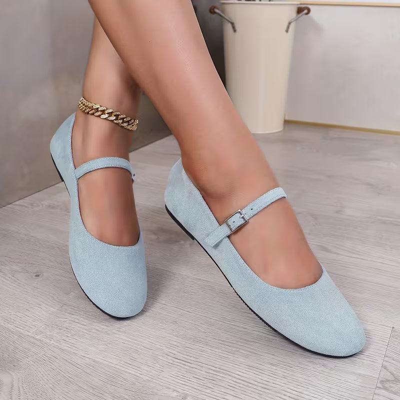 Light blue suede shoes worn by a person on a wooden floor.