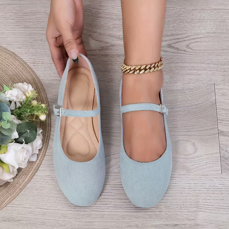 Light blue flats being held by a hand on a wooden floor with flowers in the background