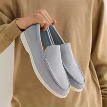 Person holding a pair of gray slip-on shoes against a neutral background