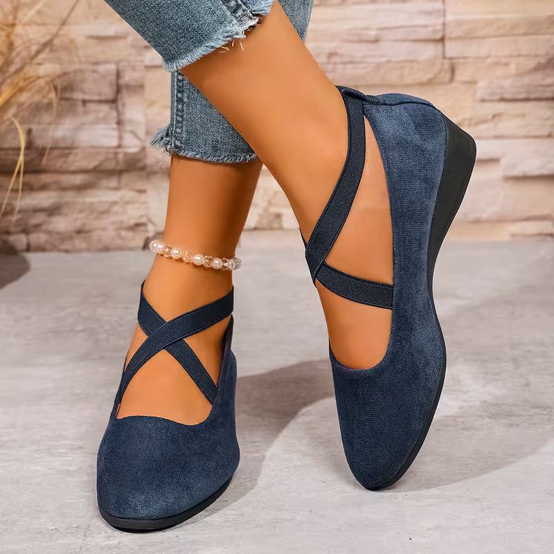 Navy blue flat shoes with criss-cross straps worn by a person on a wooden floor.
