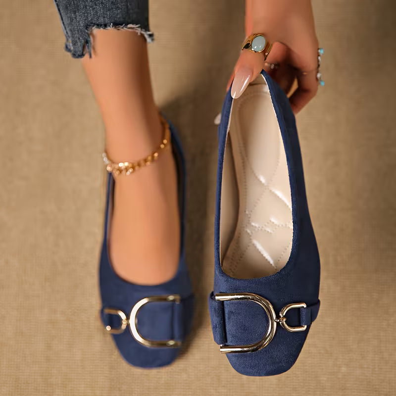 Navy blue shoes with gold buckles held by a hand on a beige background