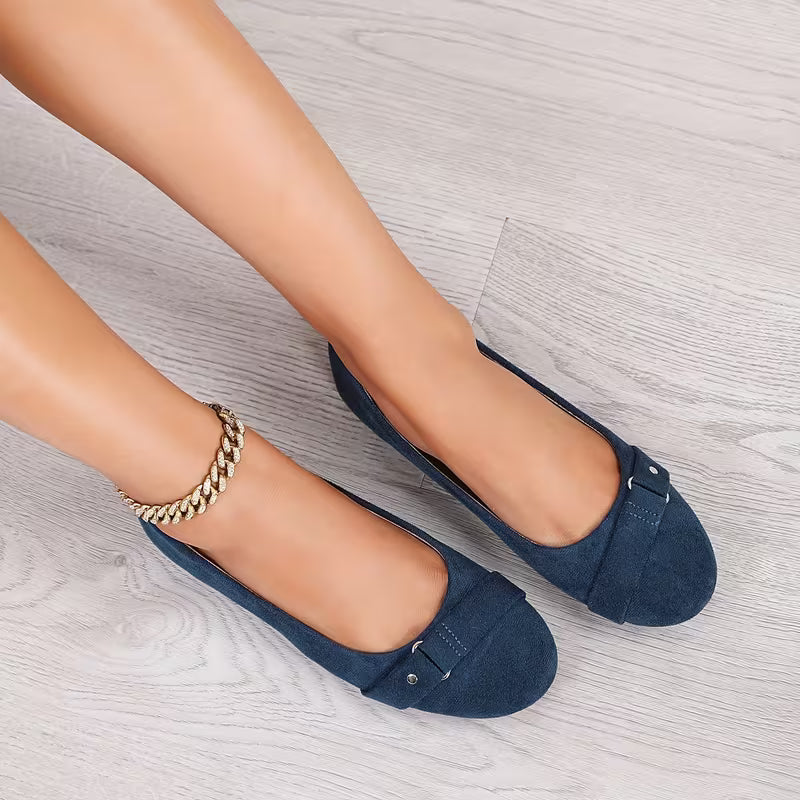 Navy blue flats worn by a person on a light gray surface