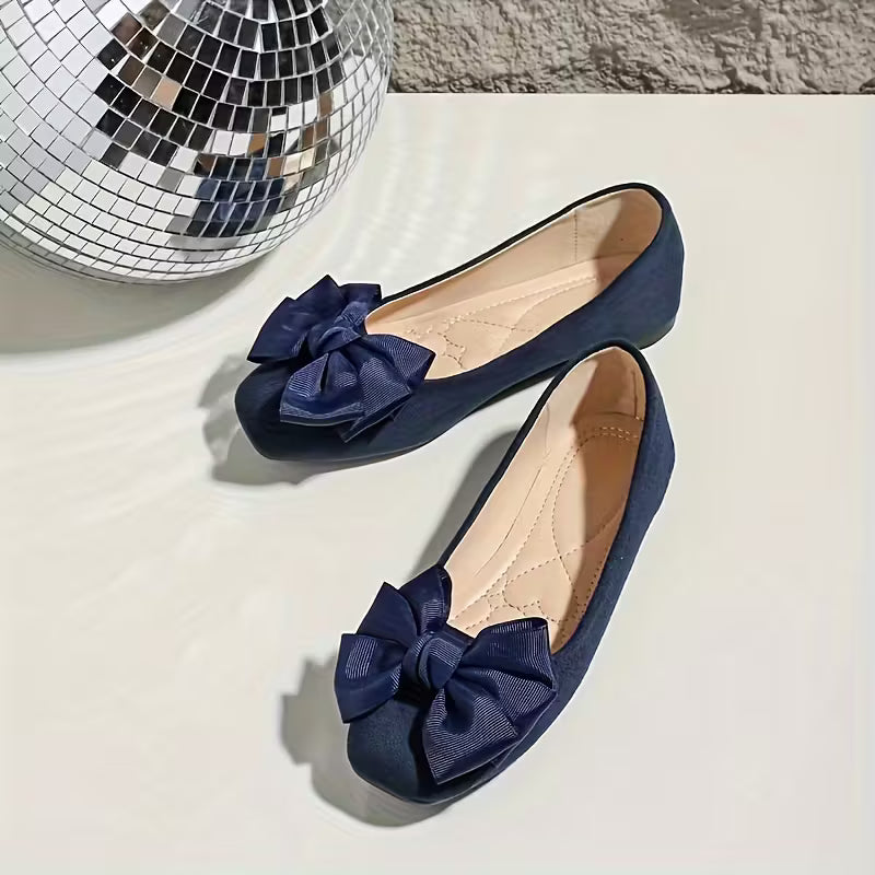 Navy blue flats with bow details on a light surface with a disco ball in the background
