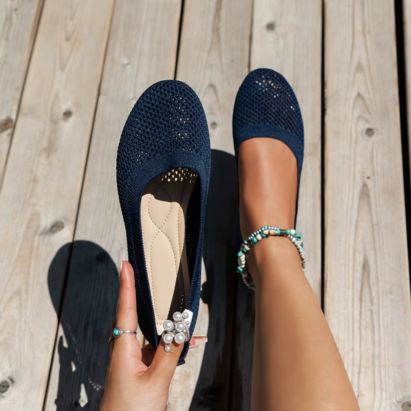 Navy blue flats worn on a wooden floor with a hand holding one flat shoe.